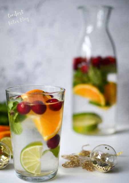 glass of infused water with citrus slices and berries with carafe in the background paleo AIP infused water christmas mocktail non alcohol drink